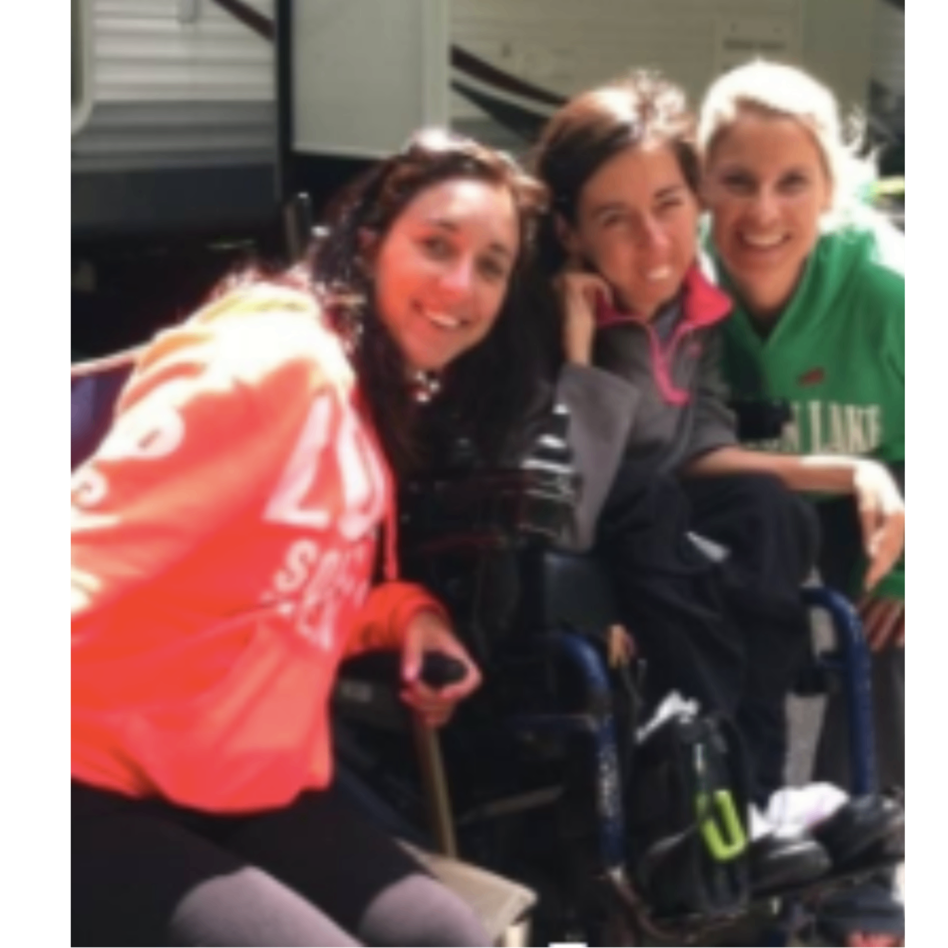 Meegan Winters with her college friend Jessica, seated in a power wheelchair, smiling outdoors with another friend.